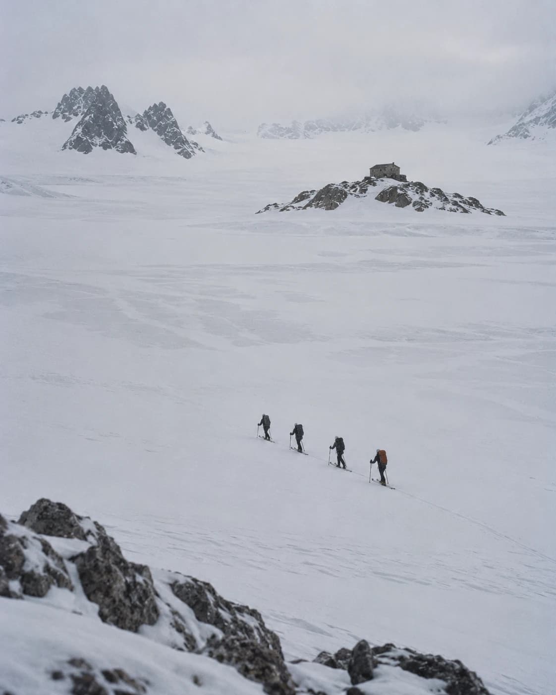 Ski tourers crossing a glacier plateau, a hut small in the distance