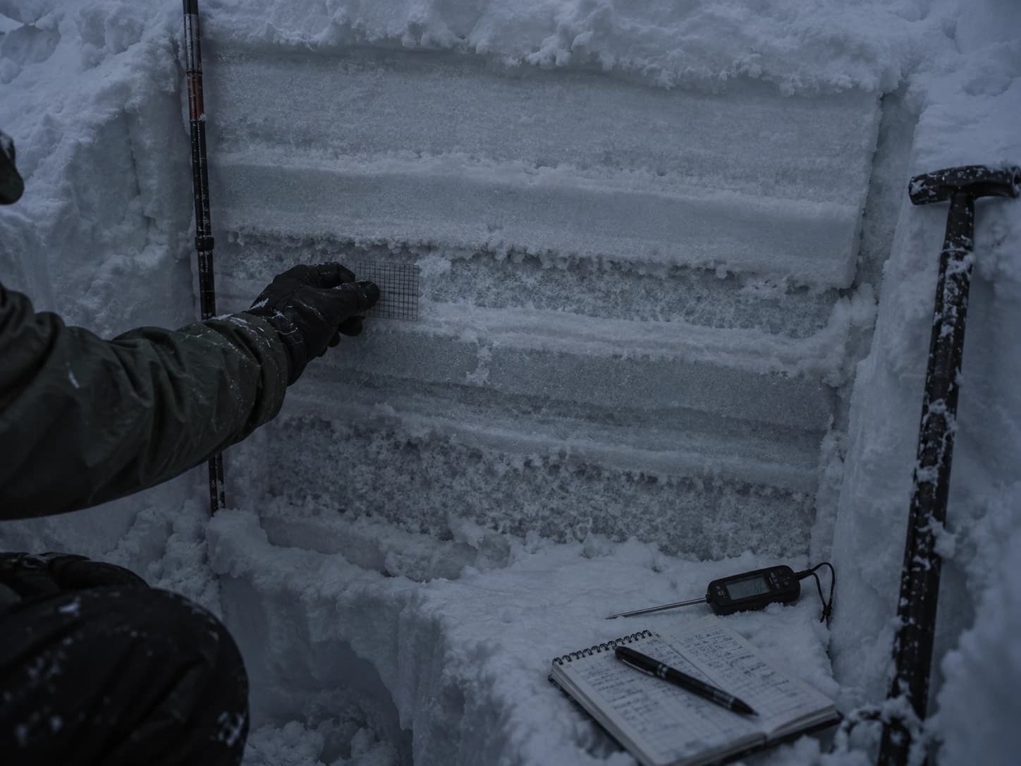 A snow pit dug into a slope, layers visible in the wall